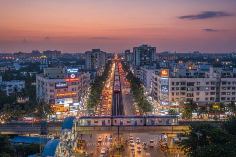 Wide road view of Medavakkam in Chennai showing residential buildings, traffic, and developing infrastructure.