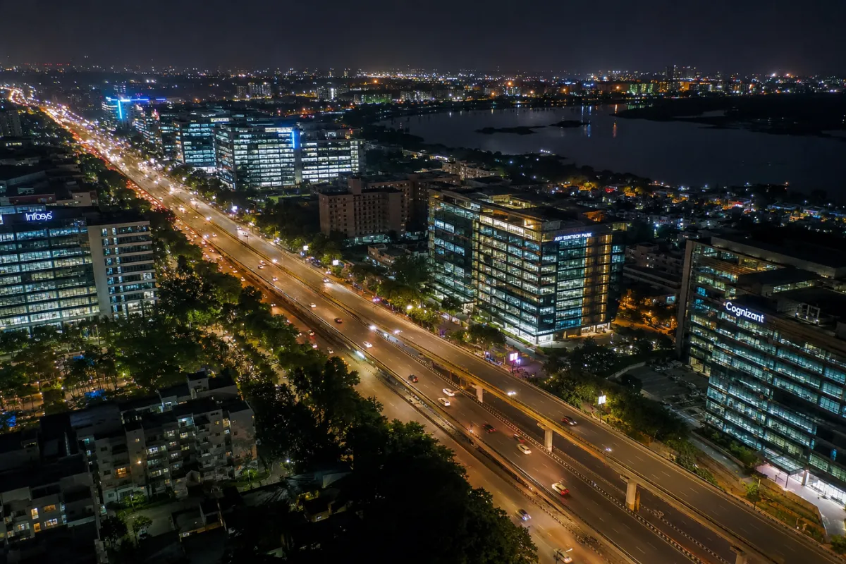 Aerial night view of Sholinganallur OMR with illuminated IT parks, office buildings, flyovers, and city traffic in Chennai.